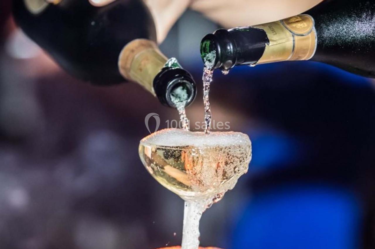 Deux bouteilles versent du champagne dans une coupe débordante, créant une mousse abondante.