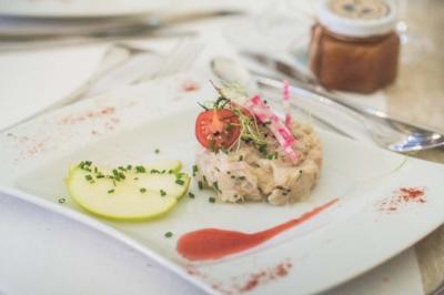Tartare de poisson servi avec une tranche de pomme, une sauce rouge, des herbes fraîches et des radis sur une assiette…