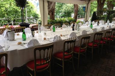 Salle lumineuse avec table ronde dressée pour un repas, nappes blanches et chaises décorées de rubans beiges.