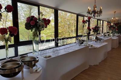 Salle lumineuse avec table ronde dressée pour un repas, nappes blanches et chaises décorées de rubans beiges.