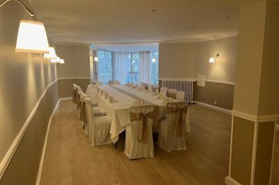 Salle lumineuse avec table ronde dressée pour un repas, nappes blanches et chaises décorées de rubans beiges.