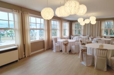 Salle lumineuse avec table ronde dressée pour un repas, nappes blanches et chaises décorées de rubans beiges.