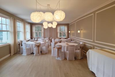 Salle lumineuse avec table ronde dressée pour un repas, nappes blanches et chaises décorées de rubans beiges.