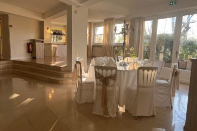 Salle lumineuse avec table ronde dressée pour un repas, nappes blanches et chaises décorées de rubans beiges.