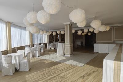 Salle lumineuse avec table ronde dressée pour un repas, nappes blanches et chaises décorées de rubans beiges.