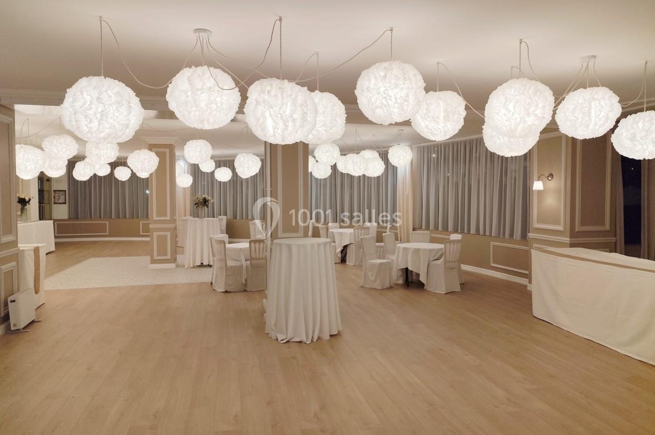 Salle de réception lumineuse avec des tables recouvertes de nappes blanches et des suspensions en papier blanc.