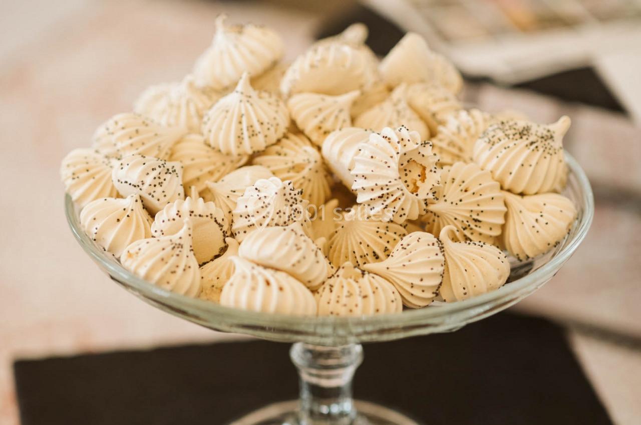 Meringues blanches décorées de graines de pavot, disposées dans une coupe en verre sur une table.
