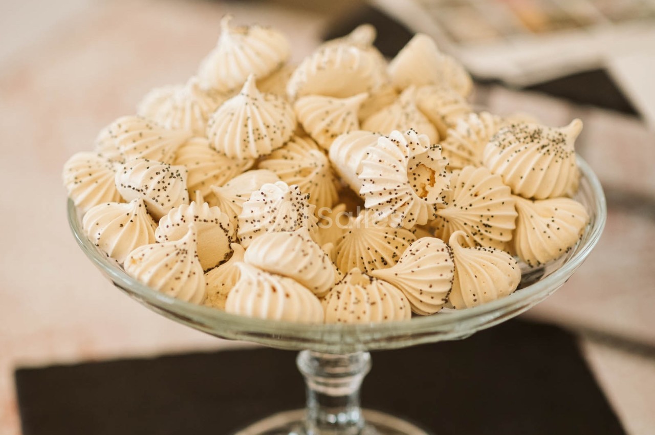 Meringues blanches décorées de graines de pavot, disposées dans une coupe en verre sur une table.
