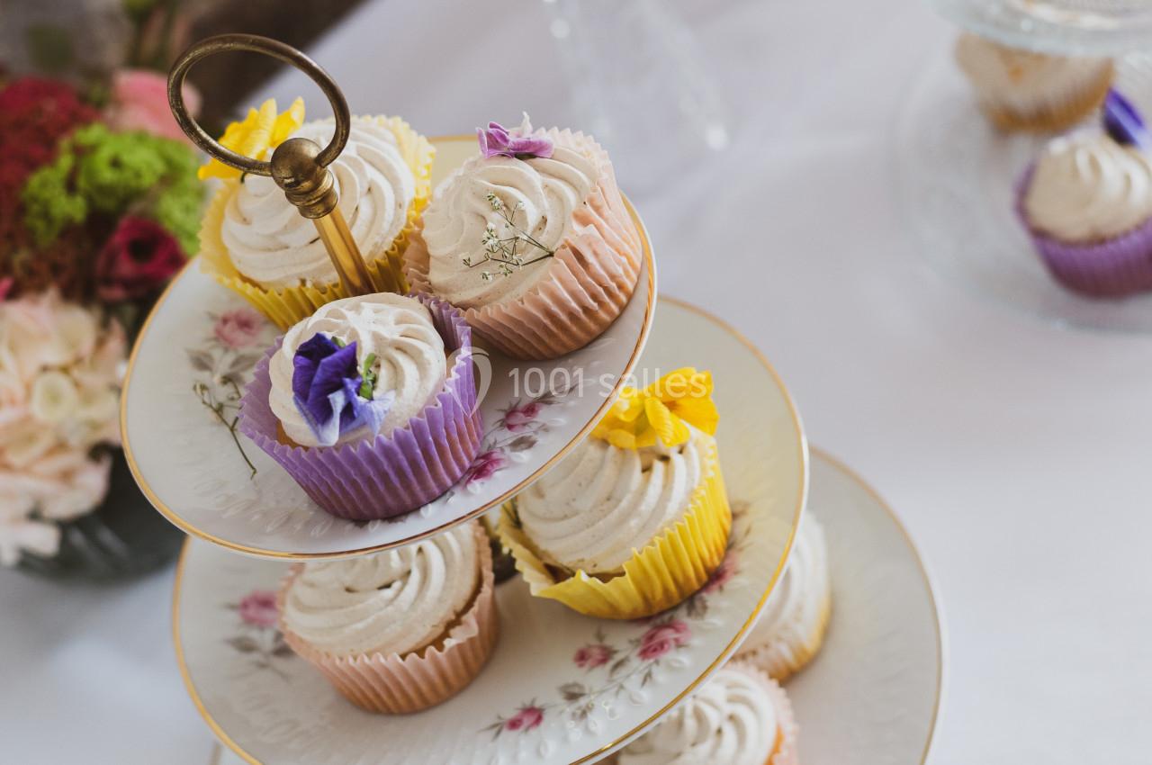Présentoir à étages avec des cupcakes décorés de fleurs comestibles, posé sur une table blanche.