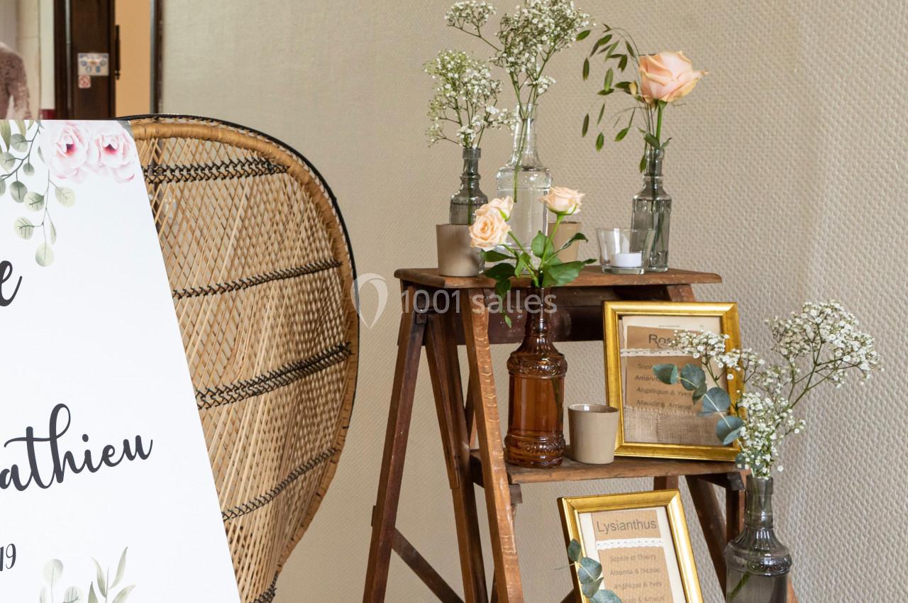 Décoration florale avec roses et gypsophiles sur des vases en verre, disposée sur une échelle en bois près d'un panneau.