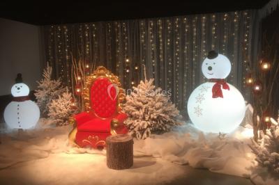 Décor hivernal avec un fauteuil rouge doré entouré de bonhommes de neige, sapins enneigés et guirlandes lumineuses.