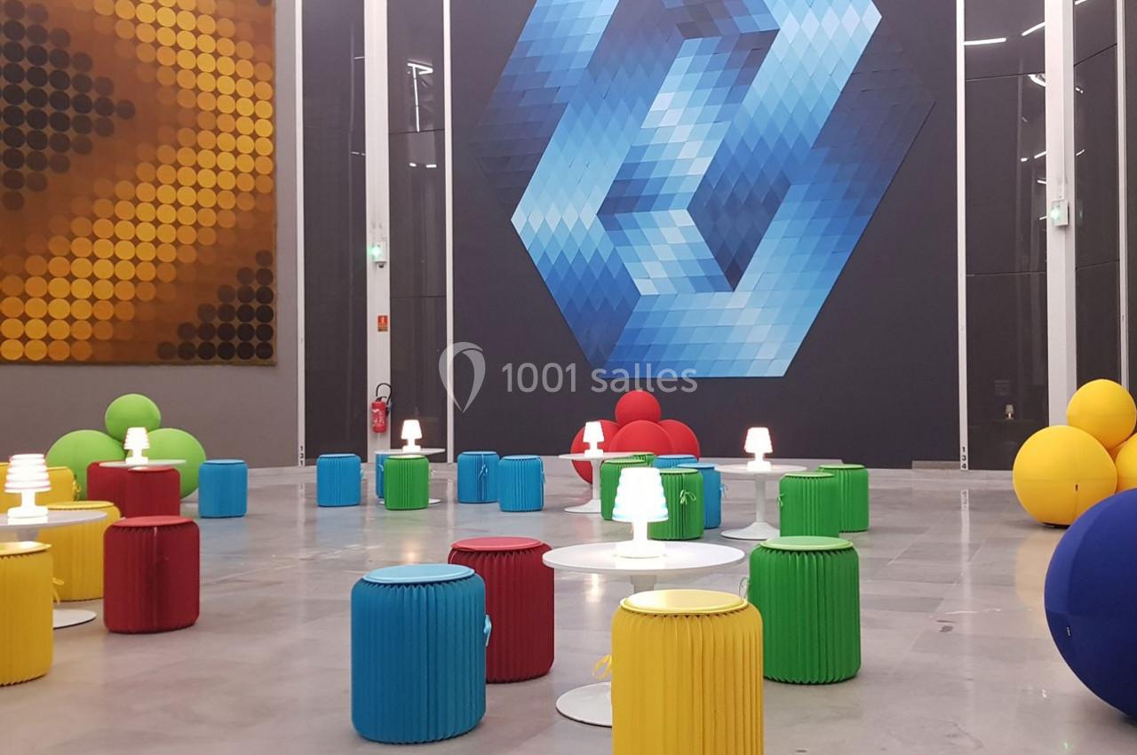 Salle moderne avec des tabourets colorés, des petites lampes blanches et des œuvres géométriques sur les murs.