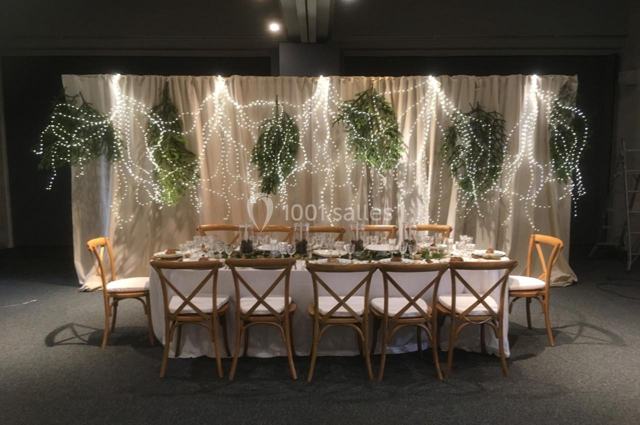 Table décorée pour un événement avec chaises en bois, nappes blanches, vaisselle élégante et guirlandes lumineuses…