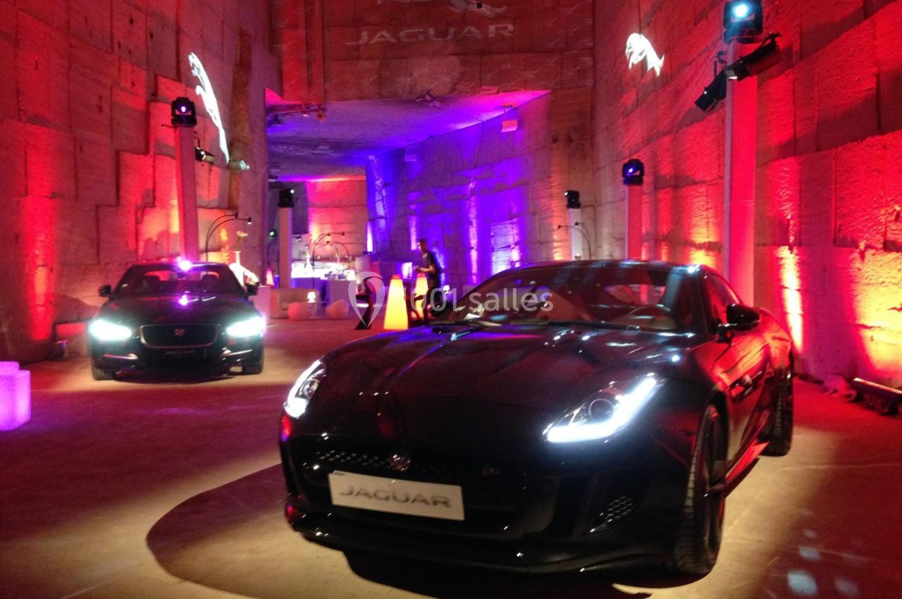 Deux voitures Jaguar exposées dans un espace intérieur éclairé par des lumières rouges et violettes.