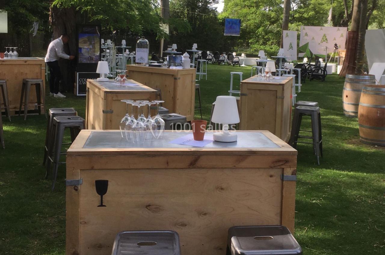 Tables en bois avec tabourets, verres et lampes disposés sur une pelouse lors d'un événement en plein air.