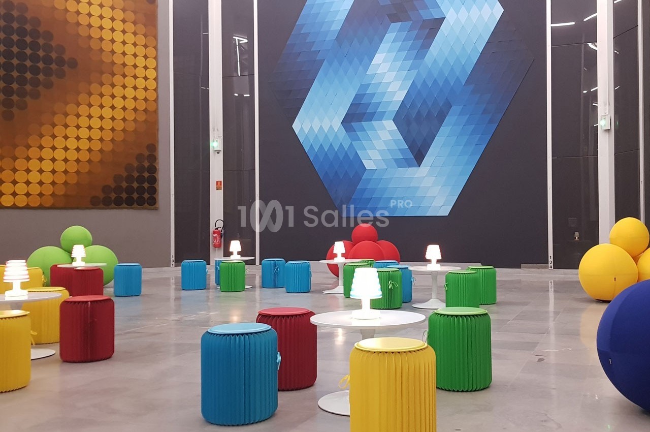 Salle moderne avec des tabourets colorés, des petites lampes blanches et des œuvres géométriques sur les murs.