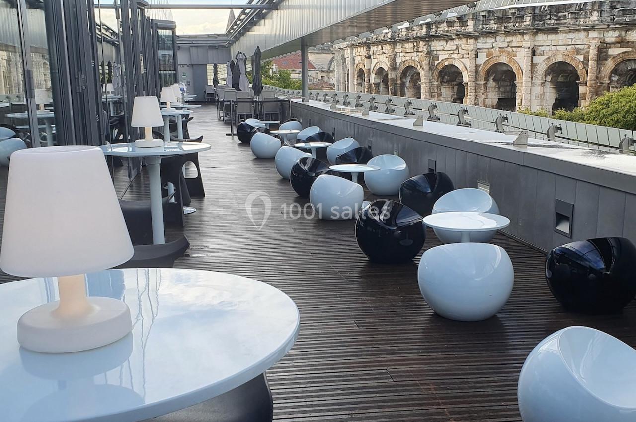 Terrasse moderne avec mobilier design, tables et sièges arrondis, vue sur un amphithéâtre ancien en arrière-plan.