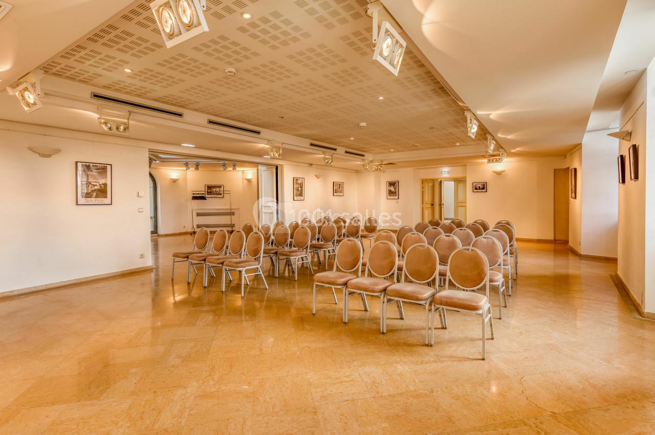 Location salle Saint-Priest (Rhône) - Château de Saint Priest #13 Salle de conférence lumineuse avec rangées de chaises beige disposées face à un espace vide, murs ornés de cadres.