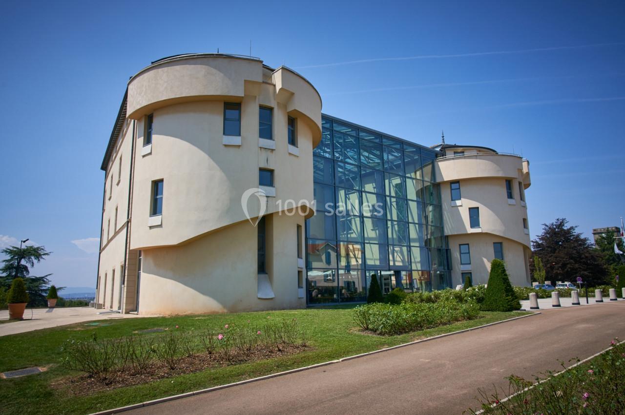 Location salle Saint-Priest (Rhône) - Château de Saint Priest #9 Bâtiment moderne avec façade en verre et murs arrondis, entouré de pelouse et d'arbustes sous un ciel bleu.