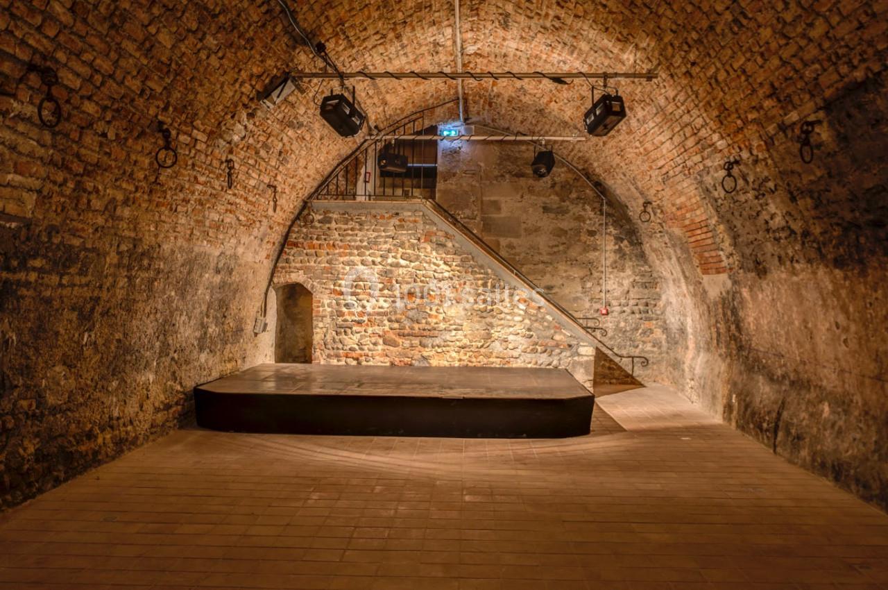 Location salle Saint-Priest (Rhône) - Château de Saint Priest #18 Salle voûtée en briques avec une petite scène surélevée, éclairée par des projecteurs suspendus.