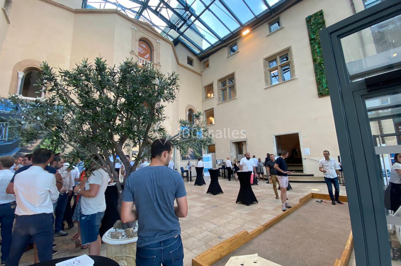 Location salle Saint-Priest (Rhône) - Château de Saint Priest #19 Personnes rassemblées dans une cour intérieure lumineuse avec un toit en verre, un terrain de pétanque et des tables hautes.
