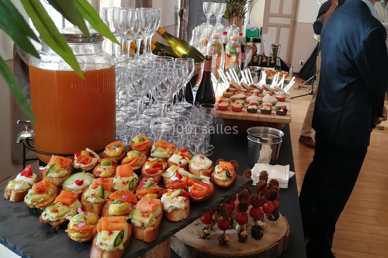 Location salle Saint-Priest (Rhône) - Château de Saint Priest #17 Buffet avec verrines, canapés variés, brochettes de fruits et jus disposés sur une table dans une salle lumineuse.
