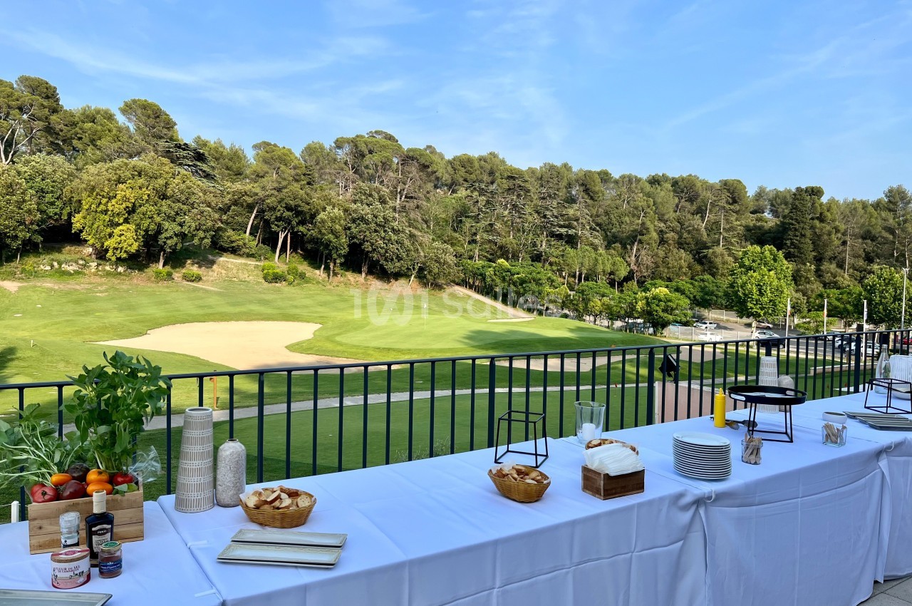 Table dressée en extérieur avec des plats et des condiments, donnant sur un terrain de golf entouré d'arbres.
