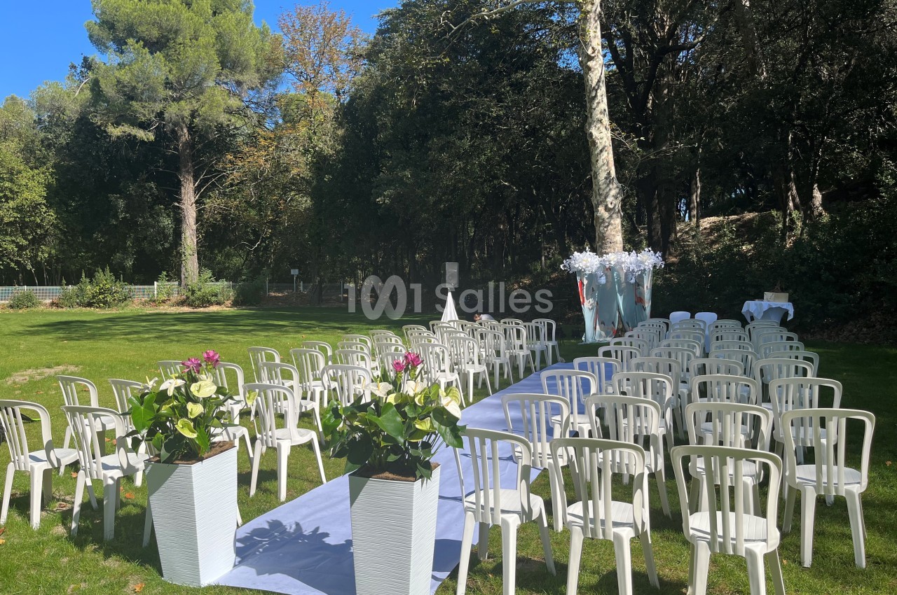 Chaises blanches disposées en rangées sur une pelouse, avec une allée centrale décorée pour une cérémonie en extérieur.