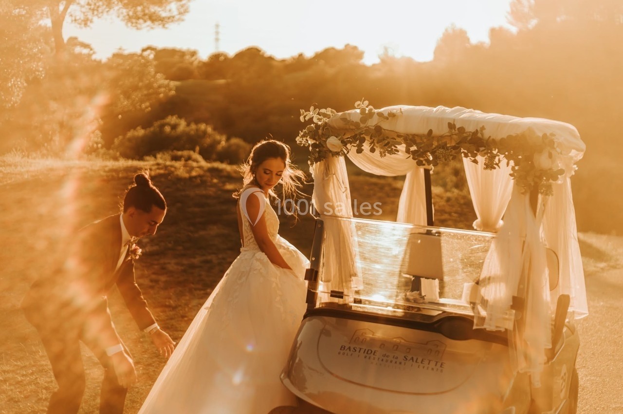 Un couple en tenue de mariage près d'une voiturette de golf décorée, éclairé par une lumière dorée au coucher du soleil.