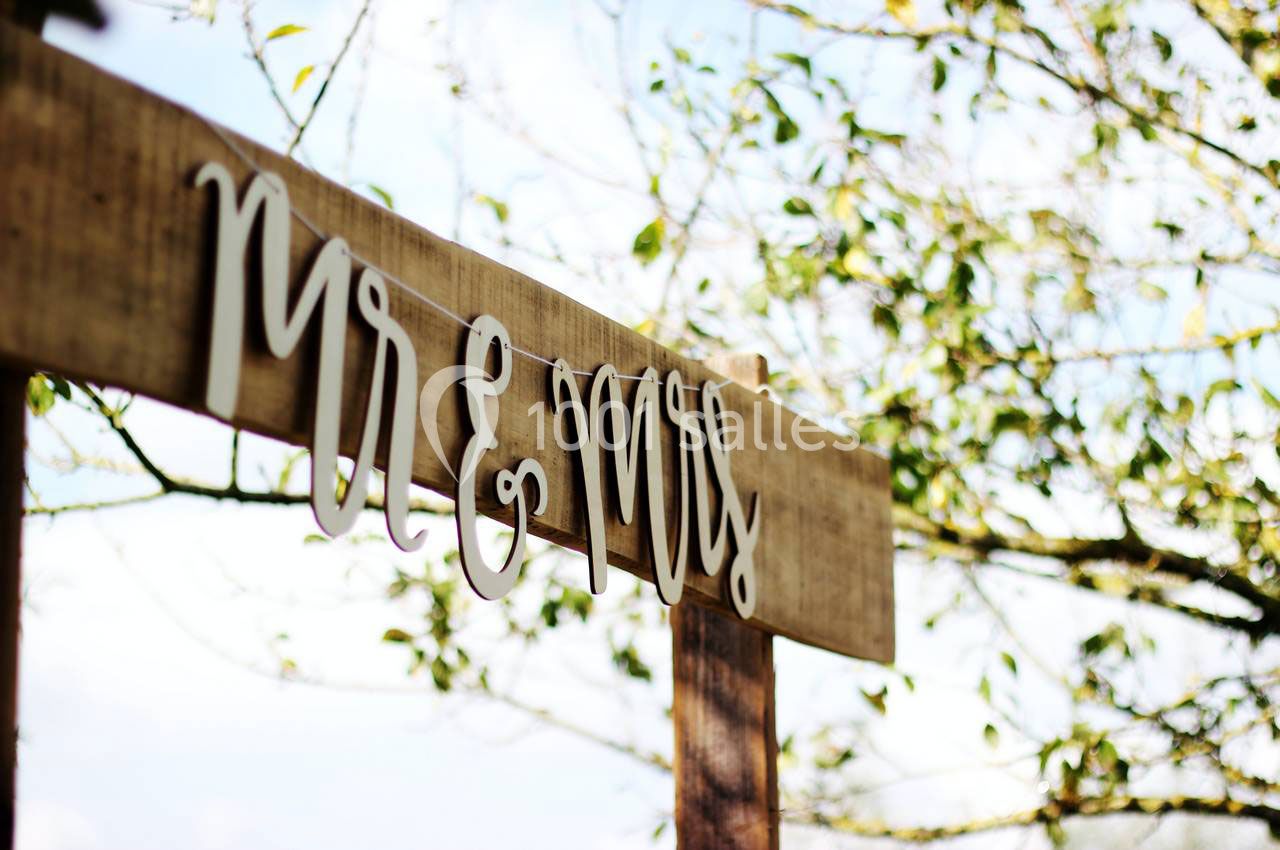 Panneau en bois suspendu avec l'inscription ’Mr & Mrs’, entouré de branches et de feuilles en arrière-plan.