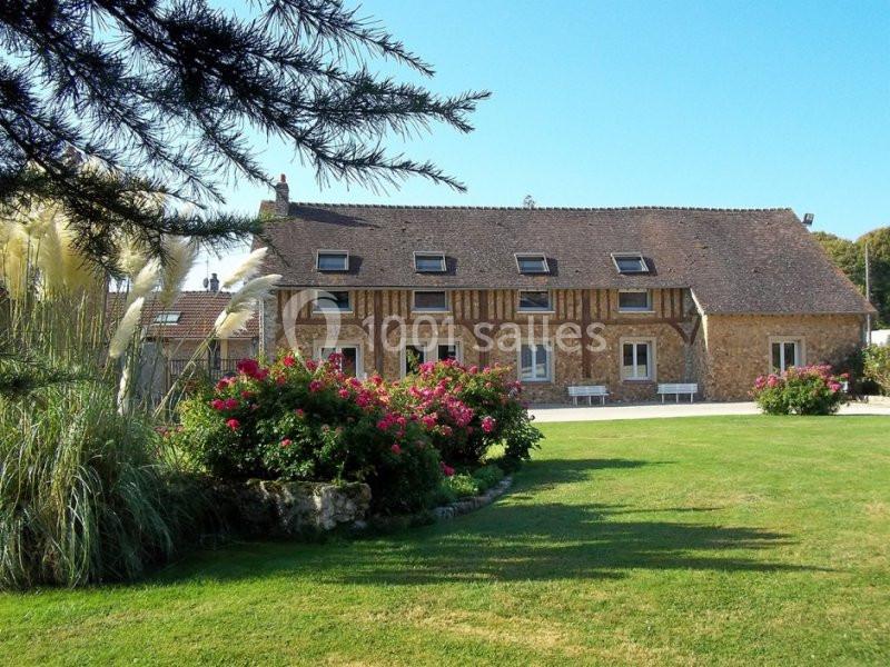 Maison en pierre et colombages entourée d'un jardin fleuri avec pelouse et arbustes sous un ciel dégagé.