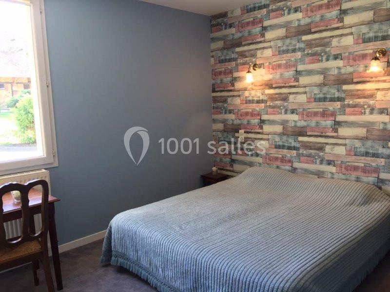 Chambre avec un lit double, mur bleu, papier peint coloré et une fenêtre donnant sur un jardin.