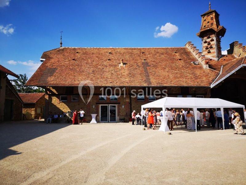 Cour d'une grande bâtisse en pierre avec toit en tuiles, des personnes rassemblées sous un barnum blanc.