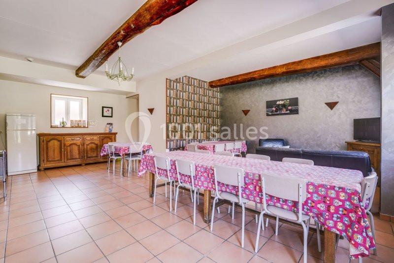 Salle à manger spacieuse avec tables alignées, nappes colorées, poutres apparentes et mobilier rustique.