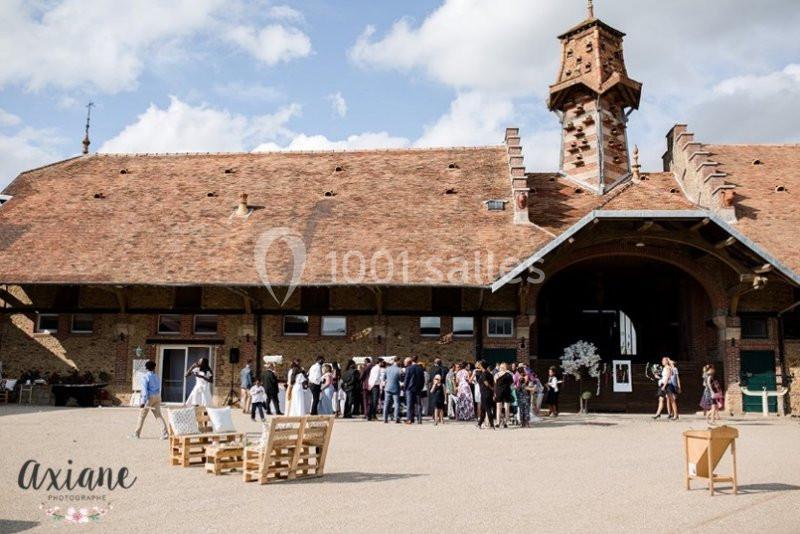 Groupe de personnes rassemblées devant un bâtiment en briques avec toit en tuiles et une petite tour.