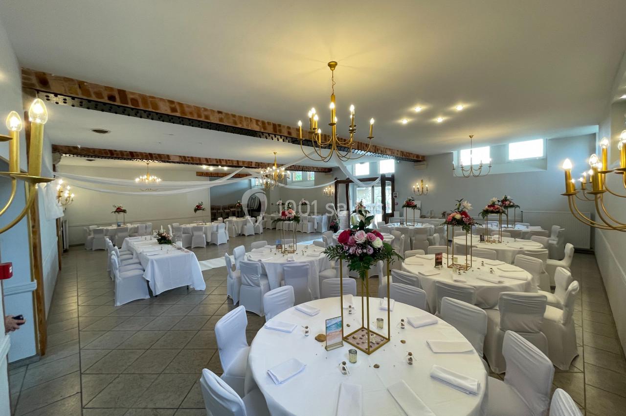Salle de réception lumineuse avec tables rondes décorées de nappes blanches et centres de table fleuris.