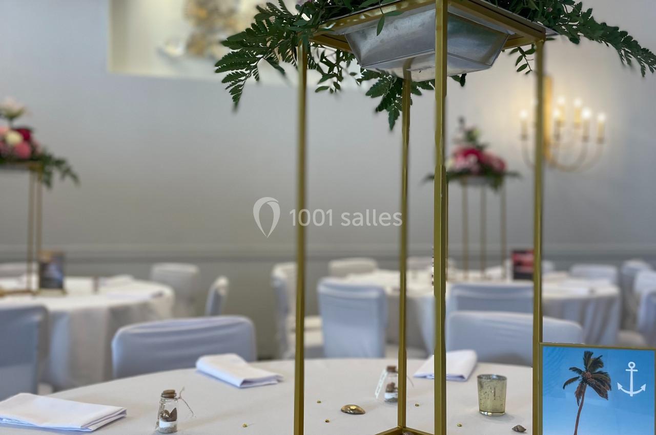 Centre de table floral avec structure dorée, décoré de fleurs roses et blanches, sur une table dressée pour un événement.