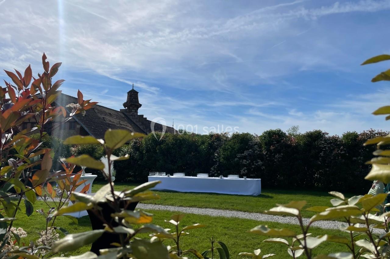 Table dressée en extérieur sur une pelouse, entourée de haies et sous un ciel bleu dégagé.