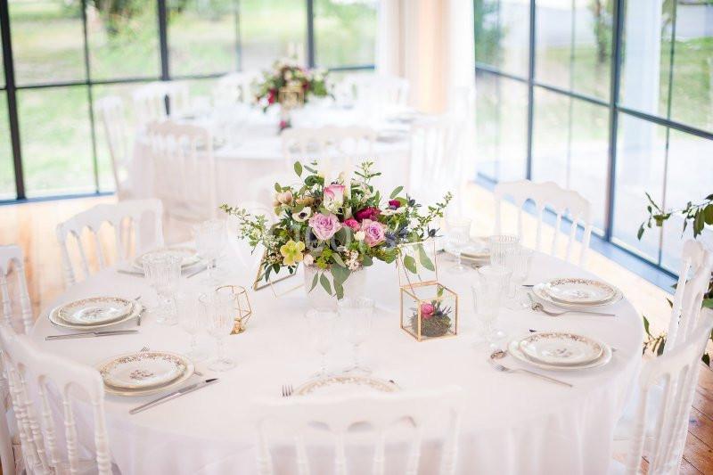 Location salle Fontains (Seine-et-Marne) - Château de Bourguignon #12 Table ronde décorée avec une nappe blanche, un centre de table floral et de la vaisselle élégante dans une salle lumineuse.