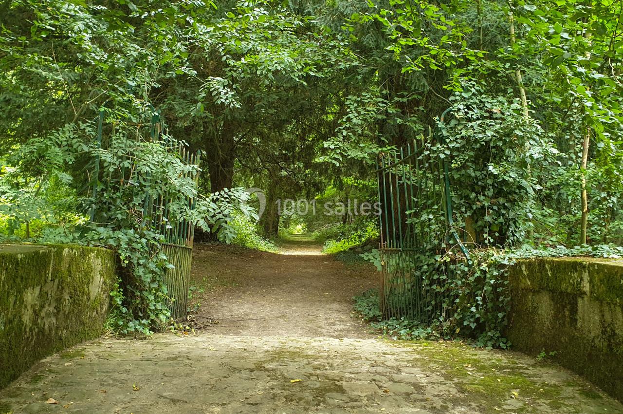 Location salle Fontains (Seine-et-Marne) - Château de Bourguignon #15 Chemin forestier traversant une arche naturelle de végétation, encadré par une barrière métallique et un pont en pierre.