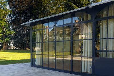 Miniature Location salle Fontains (Seine-et-Marne) - Château de Bourguignon #7 Vue nocturne d'une verrière illuminée par des lumières violettes, entourée d'arbres et d'un jardin.