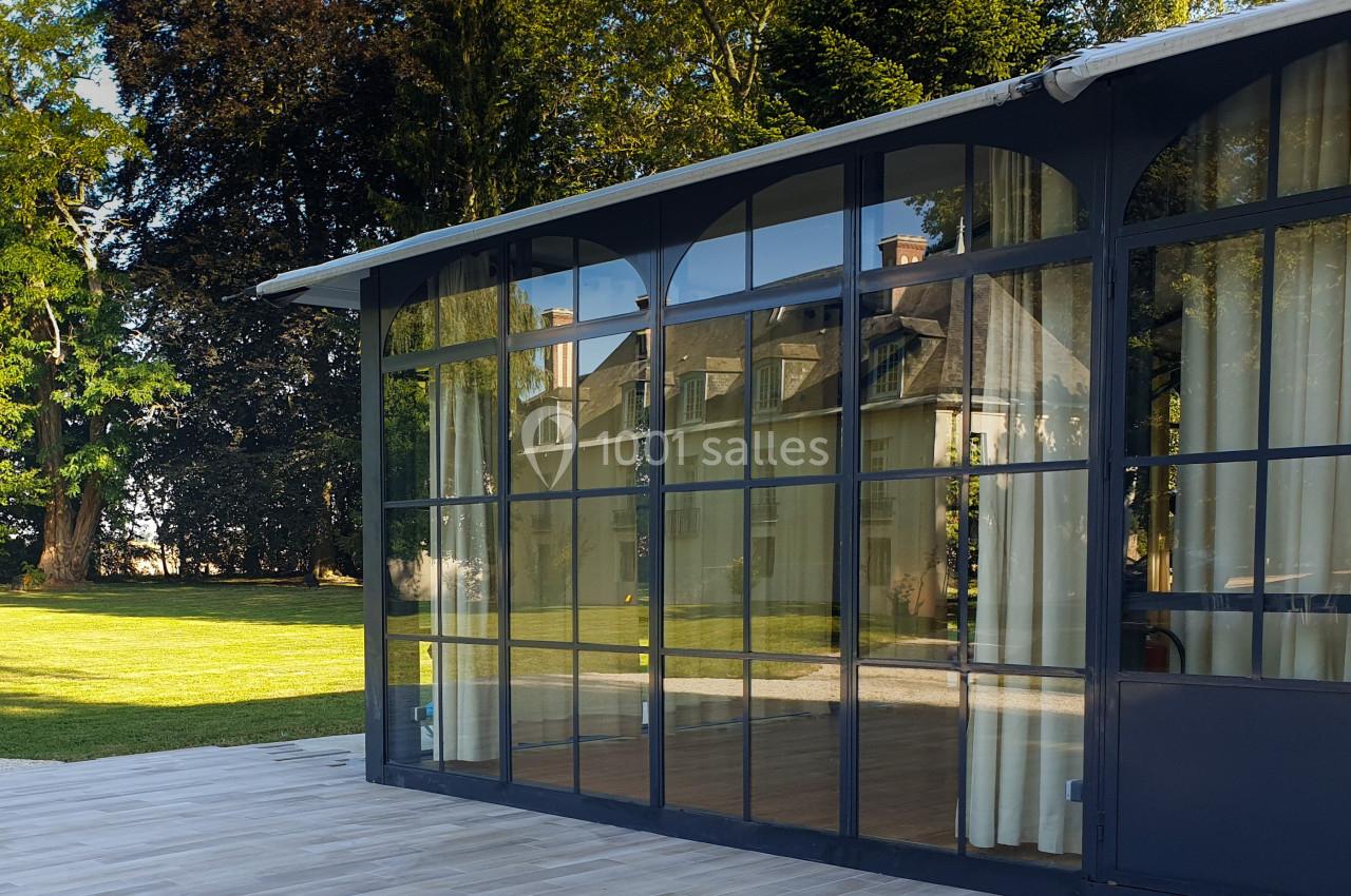 Location salle Fontains (Seine-et-Marne) - Château de Bourguignon #7 Verrière moderne donnant sur un jardin arboré, reflétant une maison ancienne sous un ciel dégagé.
