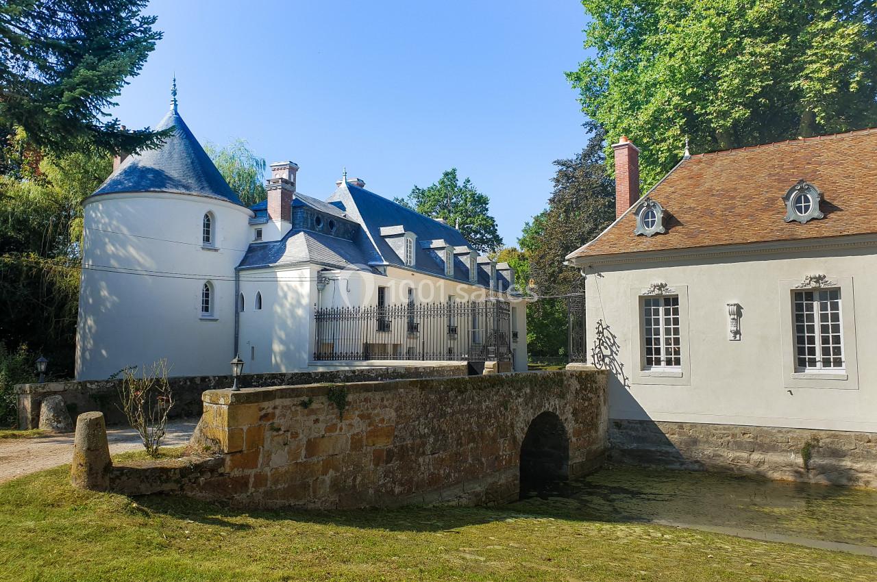 Location salle Fontains (Seine-et-Marne) - Château de Bourguignon #16 Petit château avec tourelle et dépendance, entouré d'arbres, avec un pont en pierre traversant un cours d'eau.