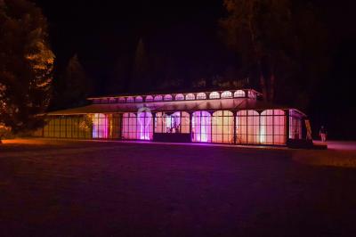 Miniature Location salle Fontains (Seine-et-Marne) - Château de Bourguignon #17 Vue nocturne d'une verrière illuminée par des lumières violettes, entourée d'arbres et d'un jardin.