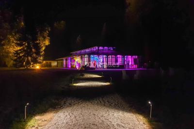 Miniature Location salle Fontains (Seine-et-Marne) - Château de Bourguignon #18 Vue nocturne d'une verrière illuminée par des lumières violettes, entourée d'arbres et d'un jardin.
