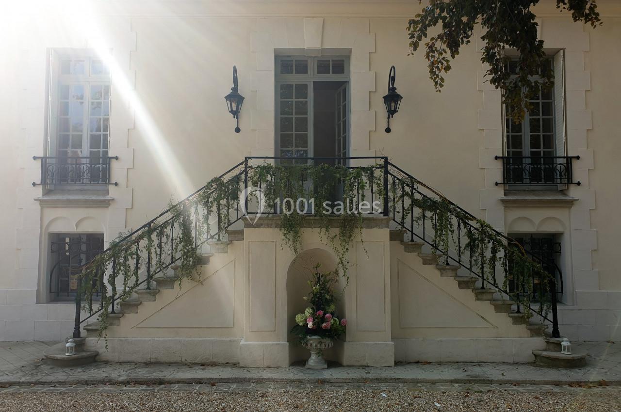 Location salle Fontains (Seine-et-Marne) - Château de Bourguignon #19 Façade d'un bâtiment avec un escalier symétrique orné de plantes grimpantes et un vase de fleurs au centre.
