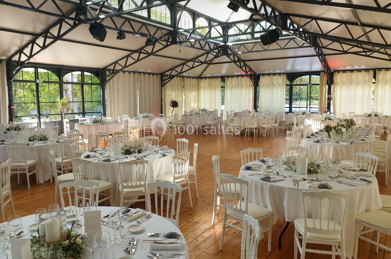Location salle Fontains (Seine-et-Marne) - Château de Bourguignon #20 Salle de réception lumineuse avec tables rondes dressées, chaises blanches et grandes baies vitrées donnant sur un espace…