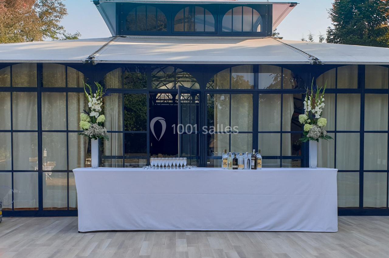 Location salle Fontains (Seine-et-Marne) - Château de Bourguignon #21 Table dressée avec nappage blanc, décorée de fleurs et disposée devant une structure vitrée dans un espace extérieur.