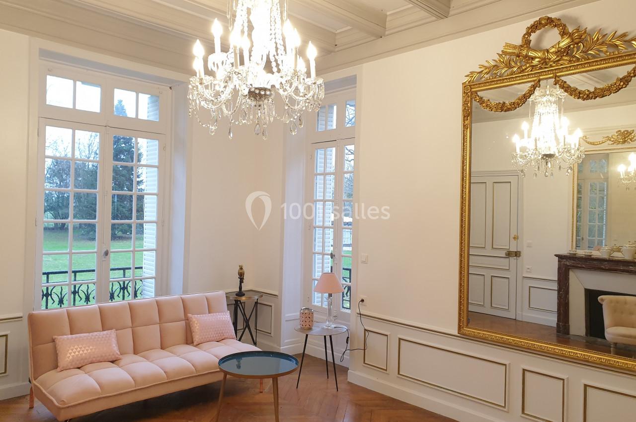 Location salle Fontains (Seine-et-Marne) - Château de Bourguignon #22 Salon lumineux avec parquet en bois, canapé rose, table basse, miroir doré et lustres en cristal.