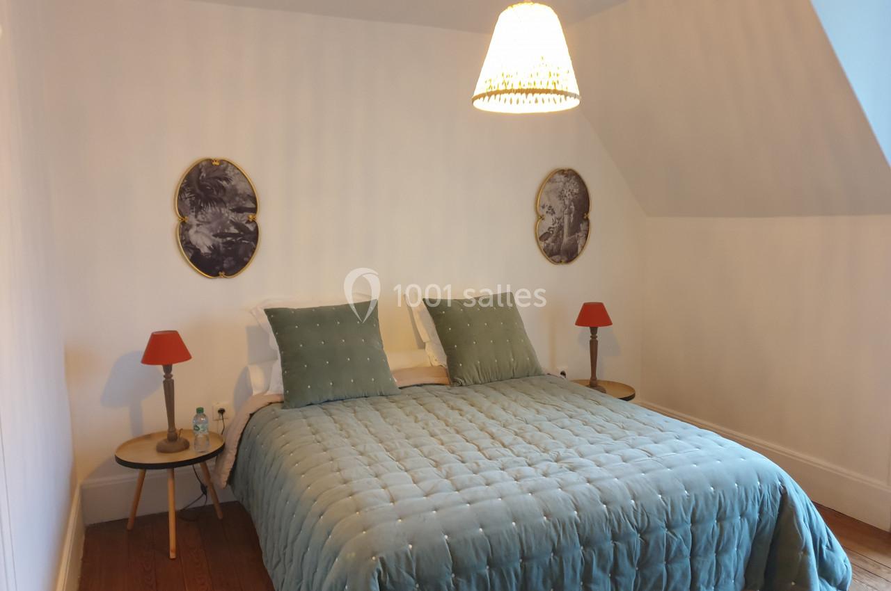 Location salle Fontains (Seine-et-Marne) - Château de Bourguignon #29 Chambre avec un lit double, couvre-lit bleu, deux tables de chevet avec lampes rouges et un lustre suspendu.